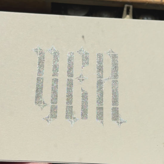 Print of the word "YEA" in a gothic typeface on a piece of gray cardstock using Tsukineko Brilliance Starlite Black ink